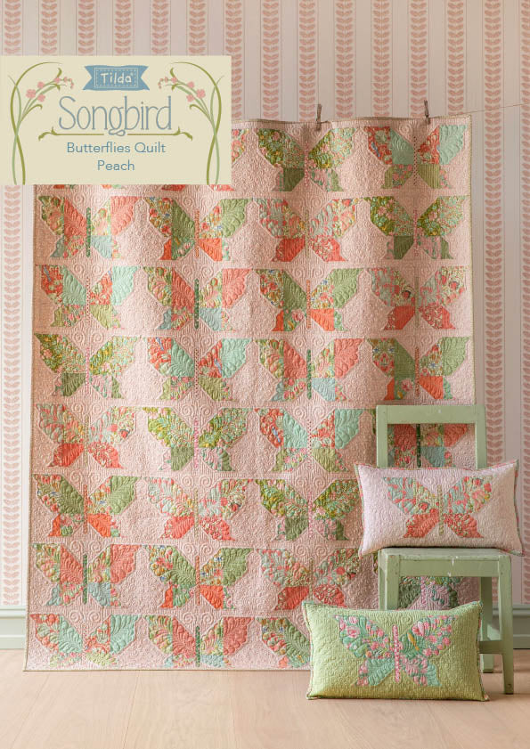 Tilda Songbird Butterfly pattern quilt with pillows on a wooden floor against striped wallpaper.