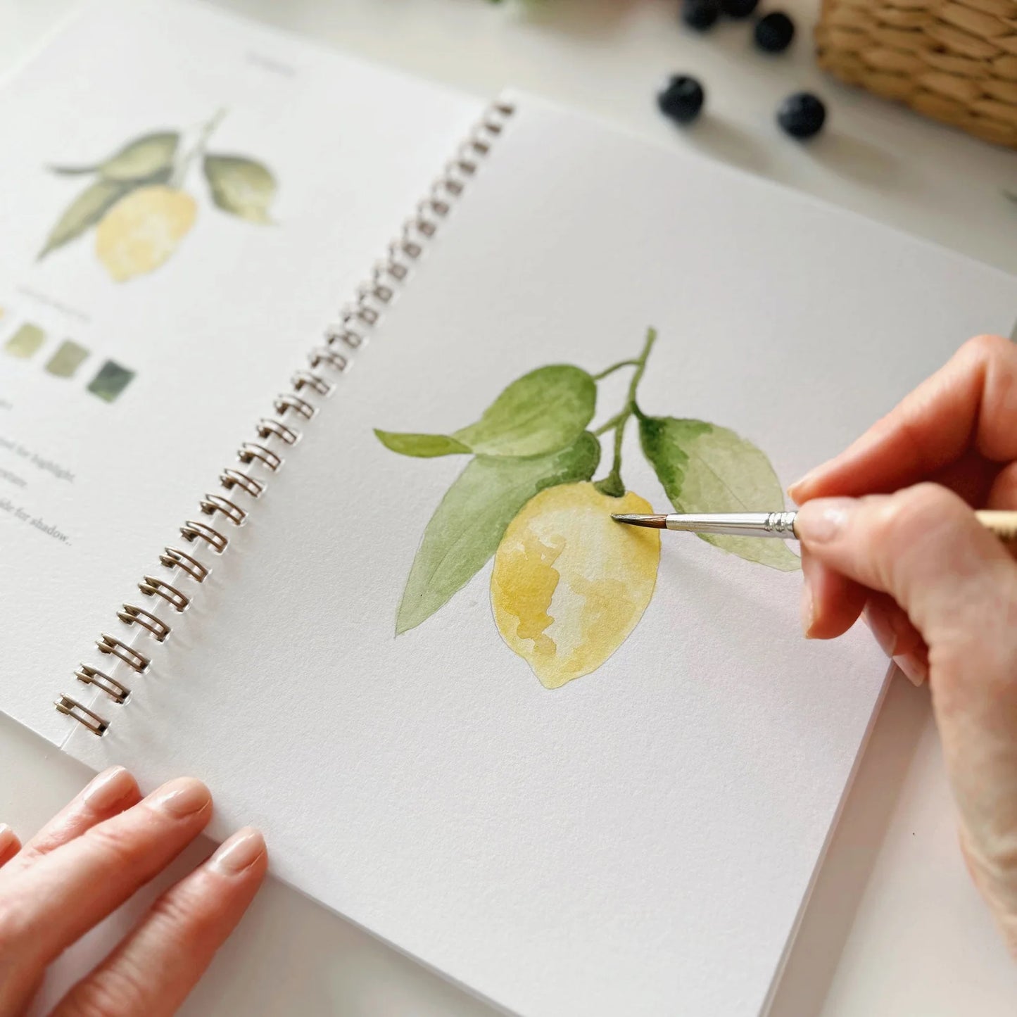 Person painting a lemon with a brush on a notebook page