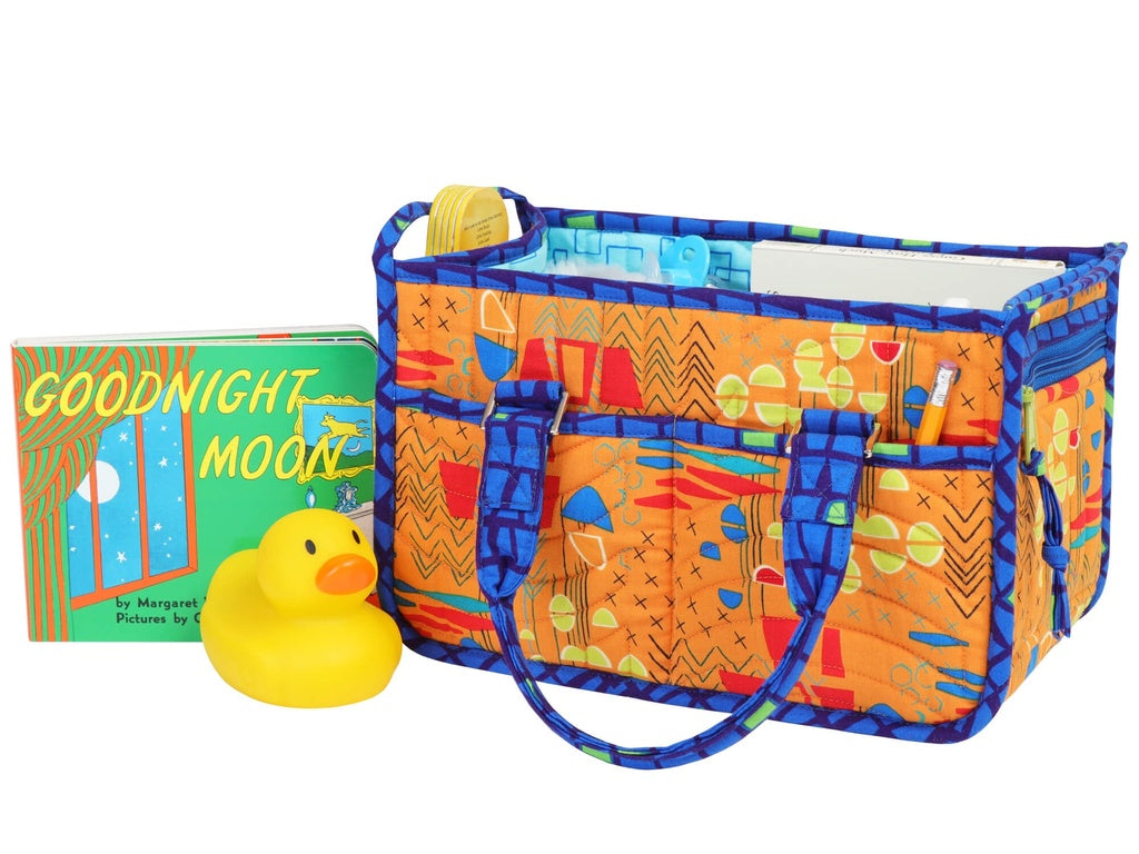 Colorful patterned baby changing bag with a rubber duck and 'Goodnight Moon' book on a white background
