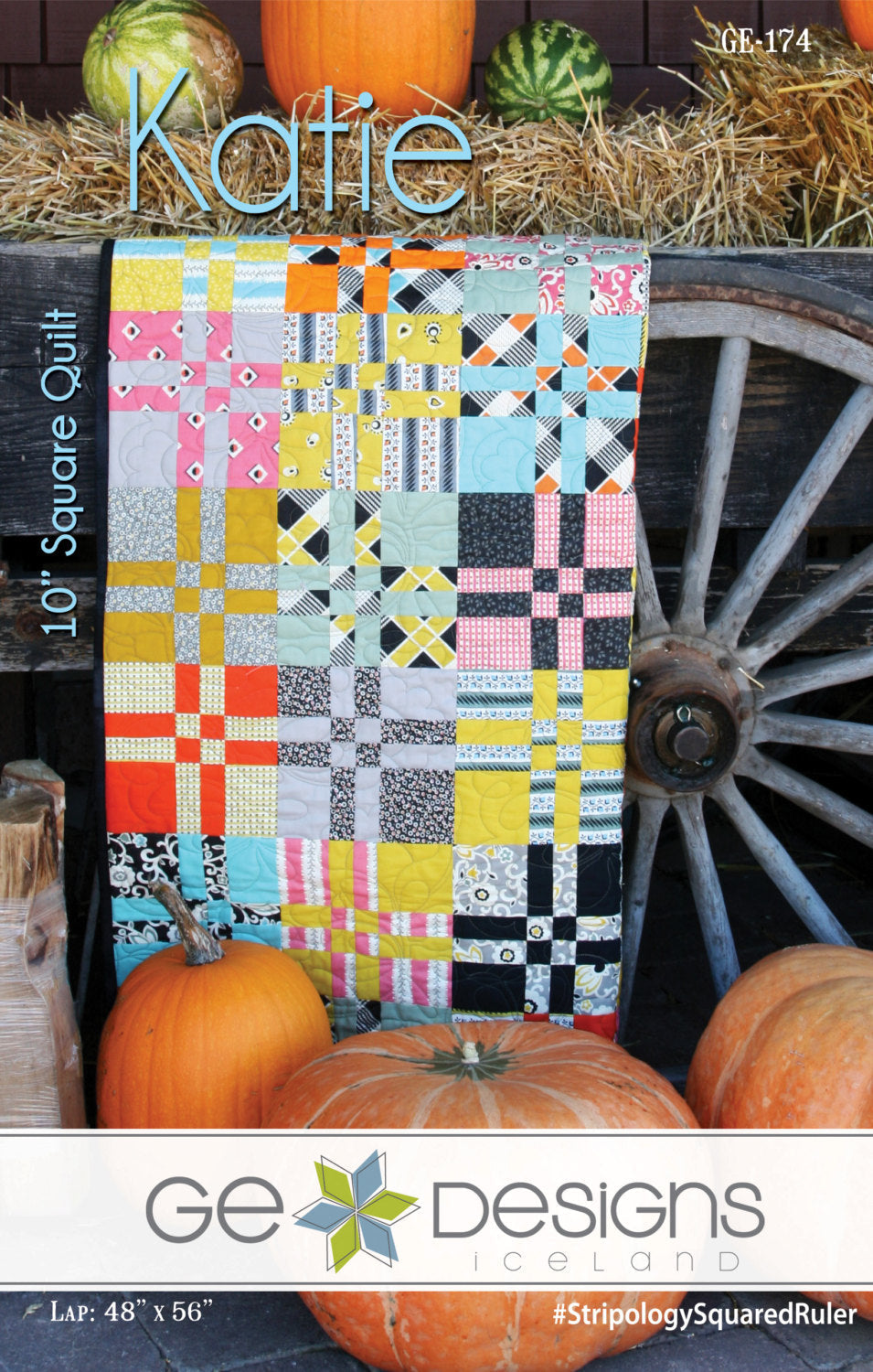 Colorful quilt with geometric pattern displayed against a rustic background with pumpkins and a wagon wheel.