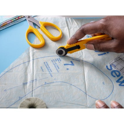 Hand using a yellow rotary cutter on fabric with sewing patterns