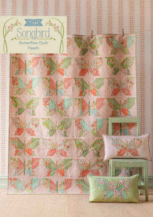 Tilda Songbird Butterfly pattern quilt with pillows on a wooden floor against striped wallpaper.