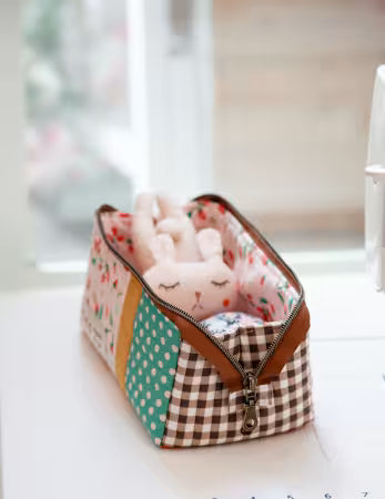 Fabric storage bag with a plush toy inside, featuring a patchwork design with polka dots and checkered patterns.