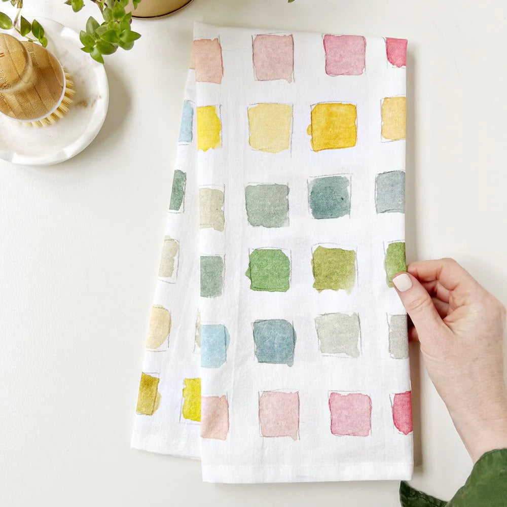 Hand holding a colorful square patterned towel on a white surface with a blurred background