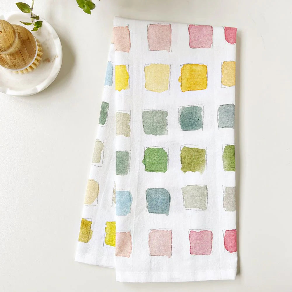 White towel with colorful square pattern on a white surface with a cup and saucer.