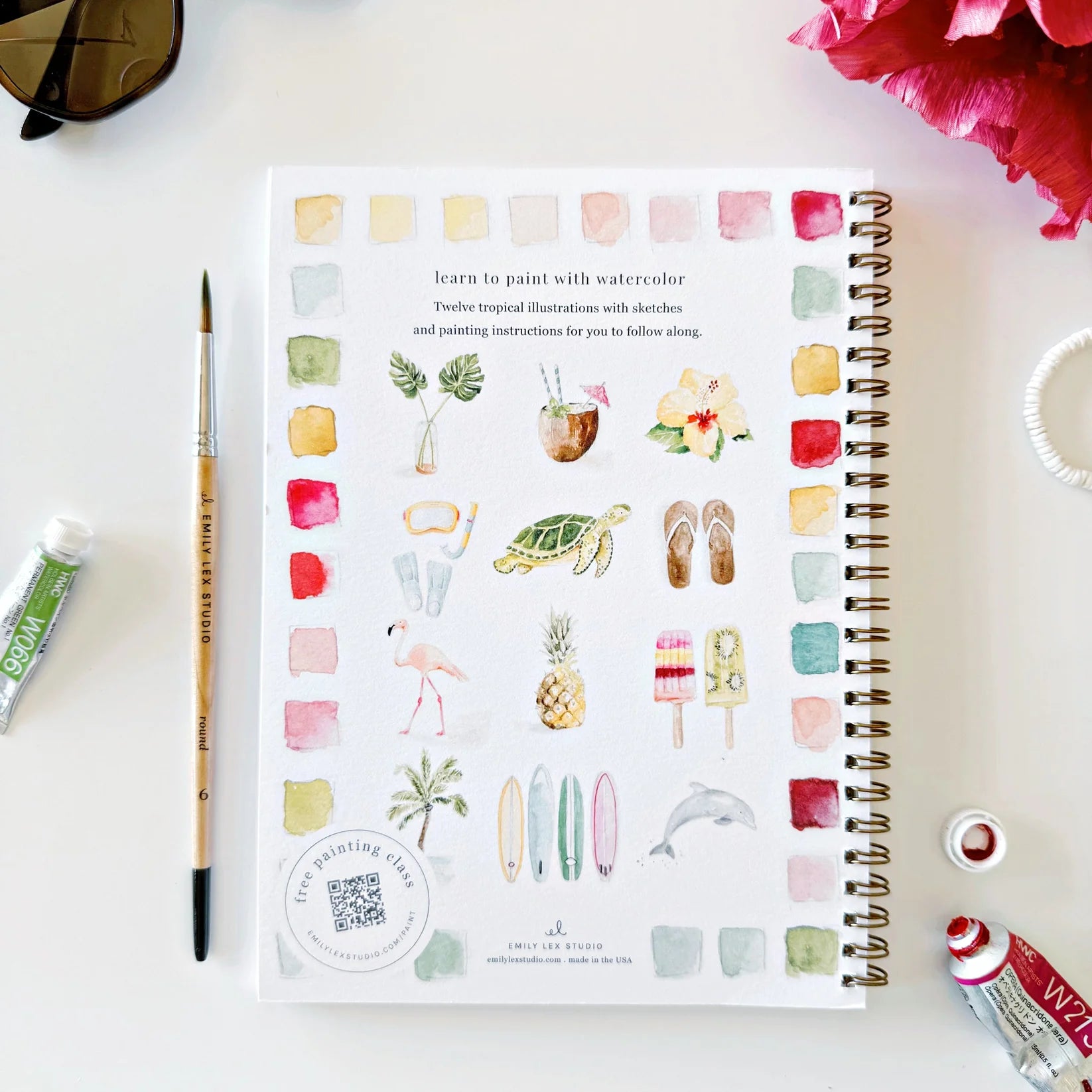 Artistic book with watercolor illustrations on a white surface with art supplies.