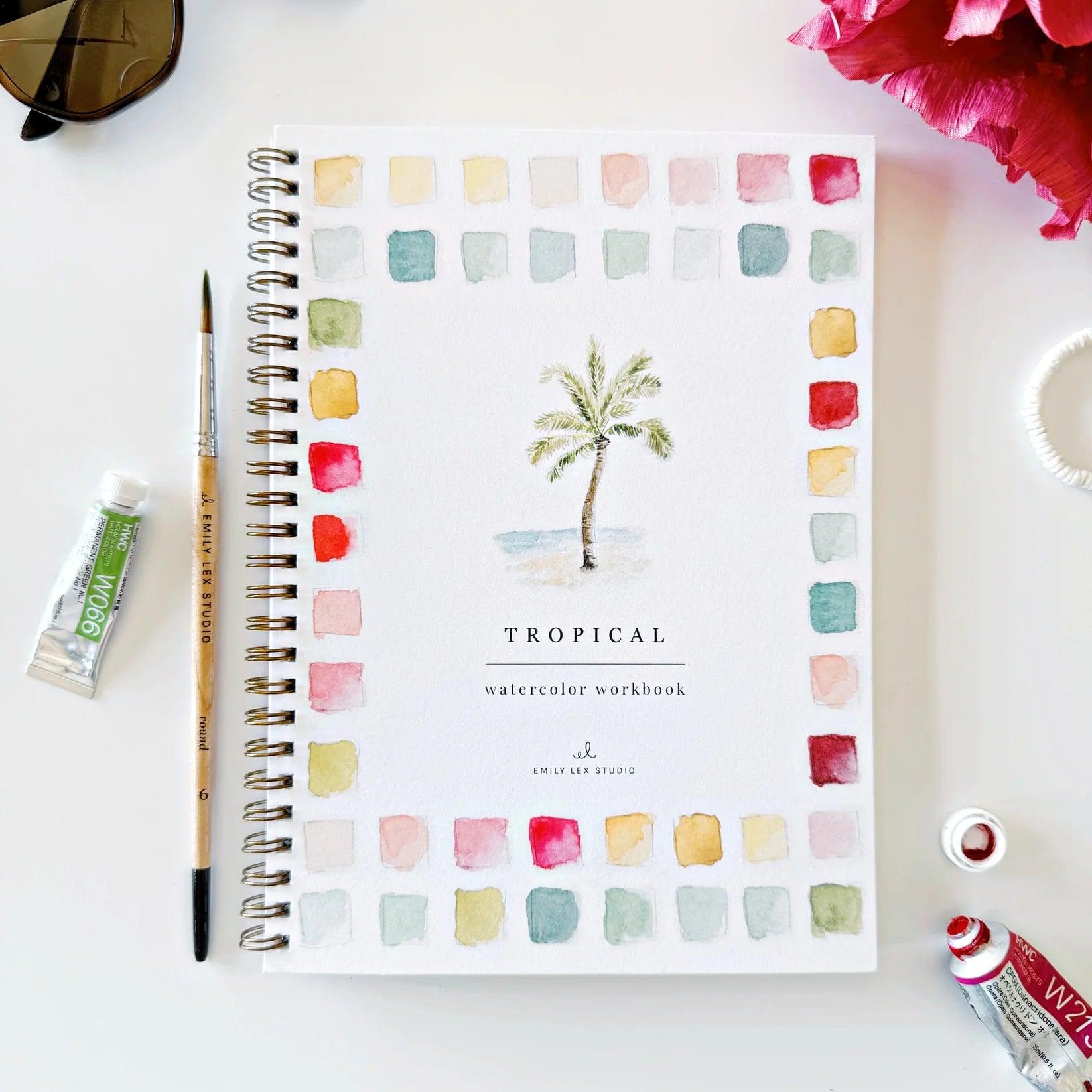 Tropical watercolor workbook with a paintbrush and ink bottle on a white surface