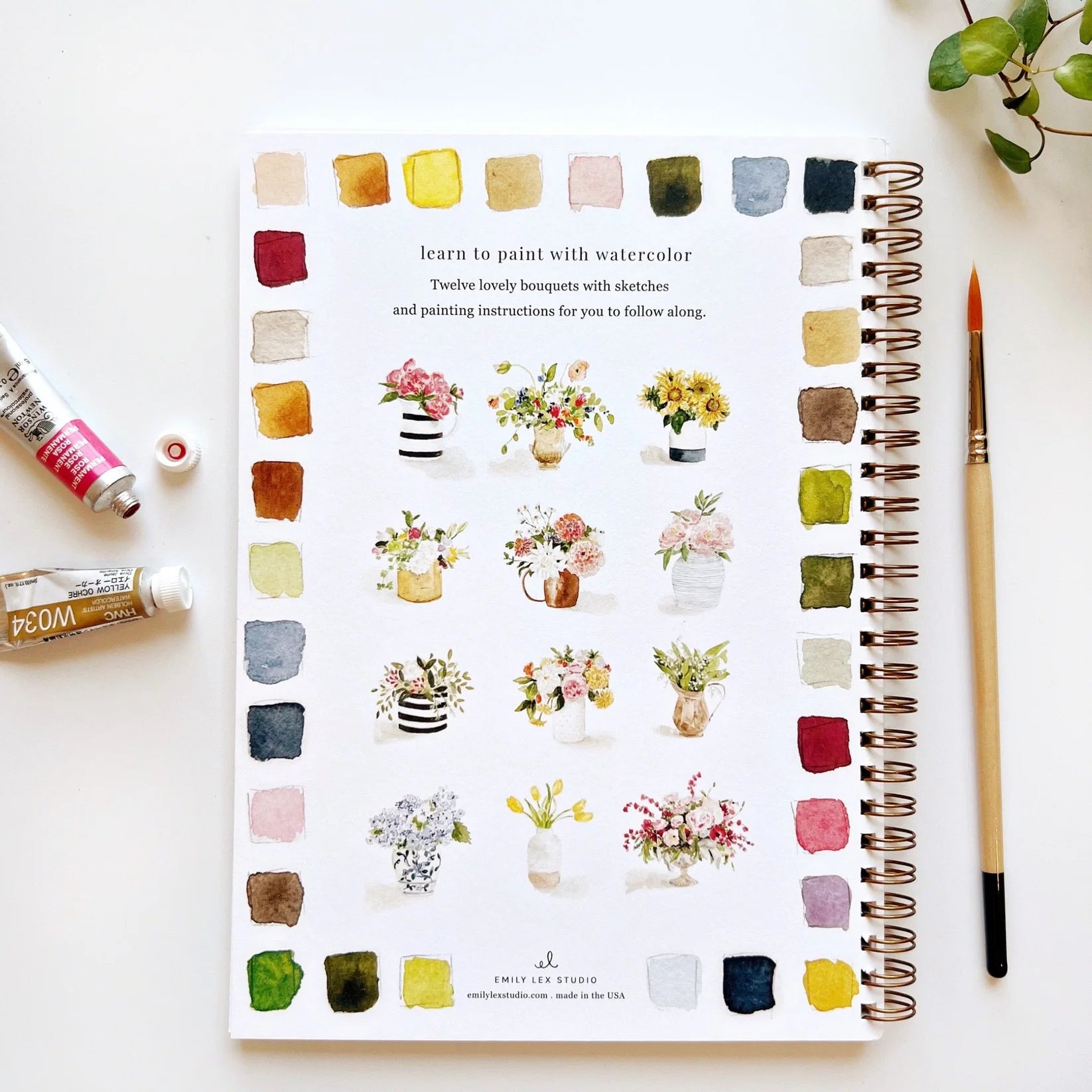 Art book with watercolor illustrations of flowers and painting tools on a white surface