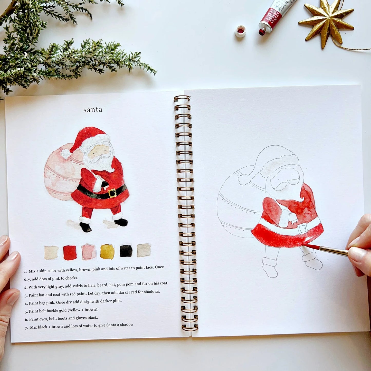 Artbook with Santa Claus illustration and painting guide on a white surface.