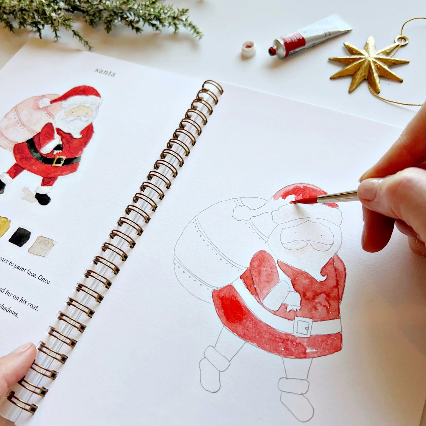 Person coloring a Santa Claus illustration in a notebook with a paintbrush.