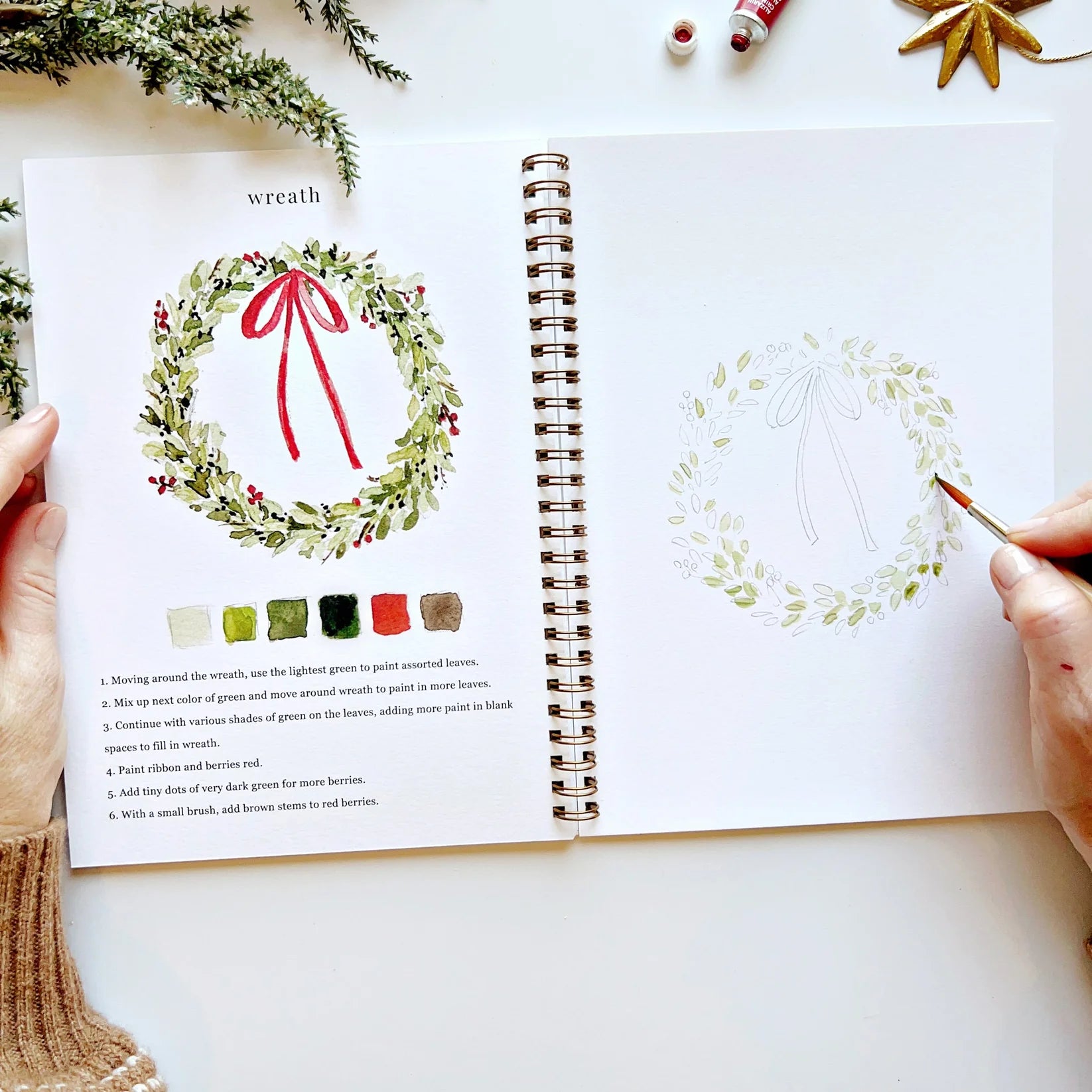 Open book with illustrations of wreaths and color swatches on a white surface.