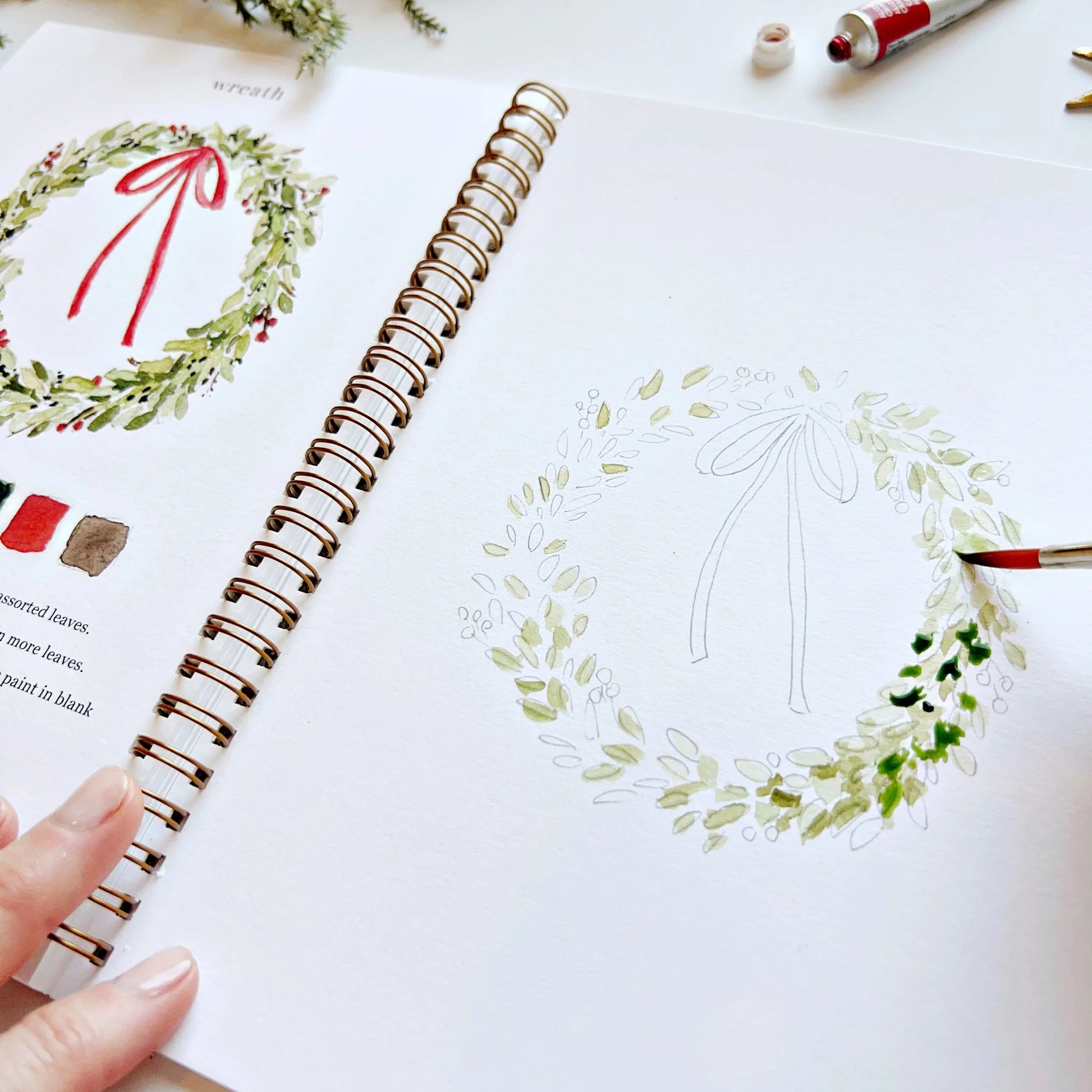 Hand holding a pen over a drawing of a wreath in a notebook