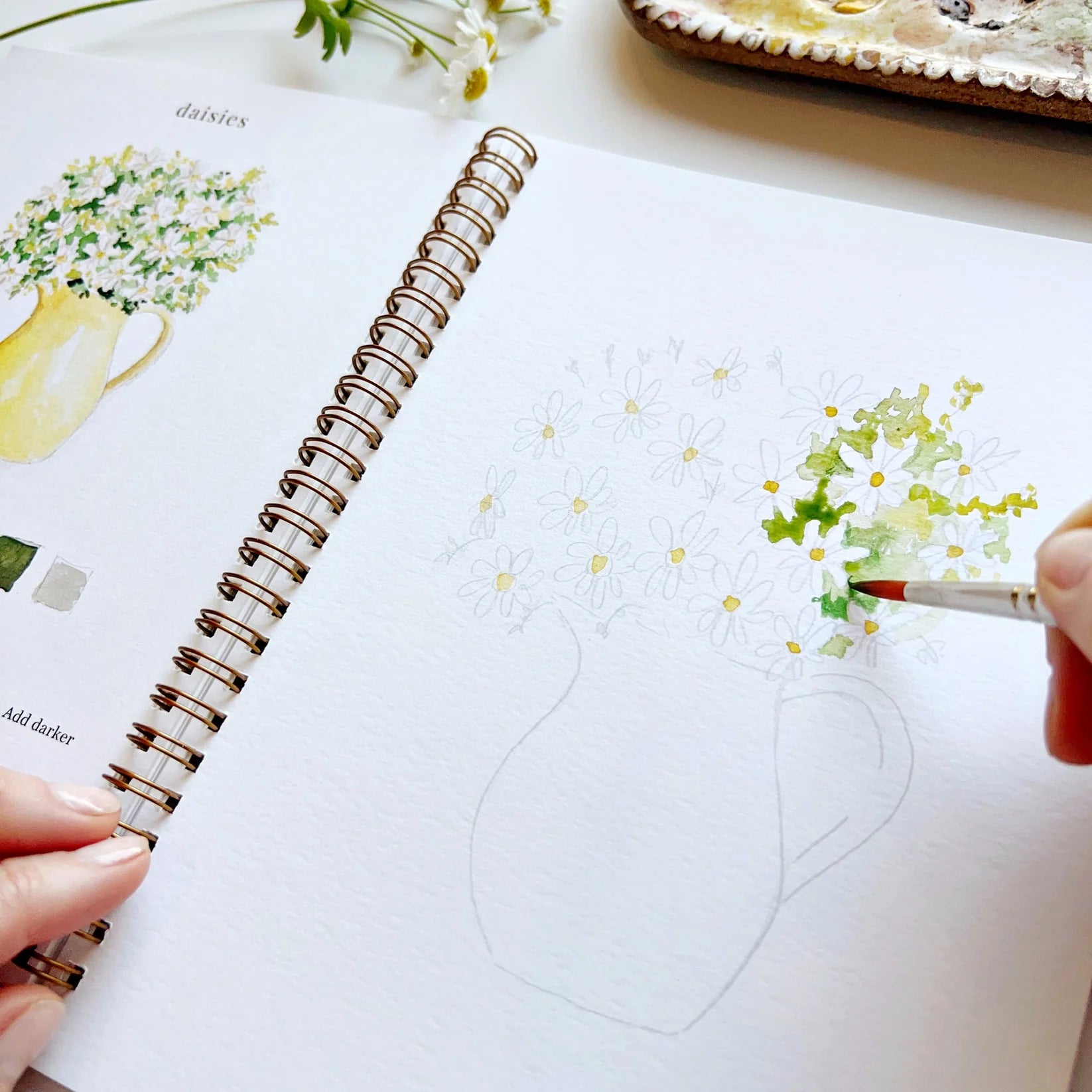 Person coloring a floral design in a spiral-bound notebook with a paintbrush.