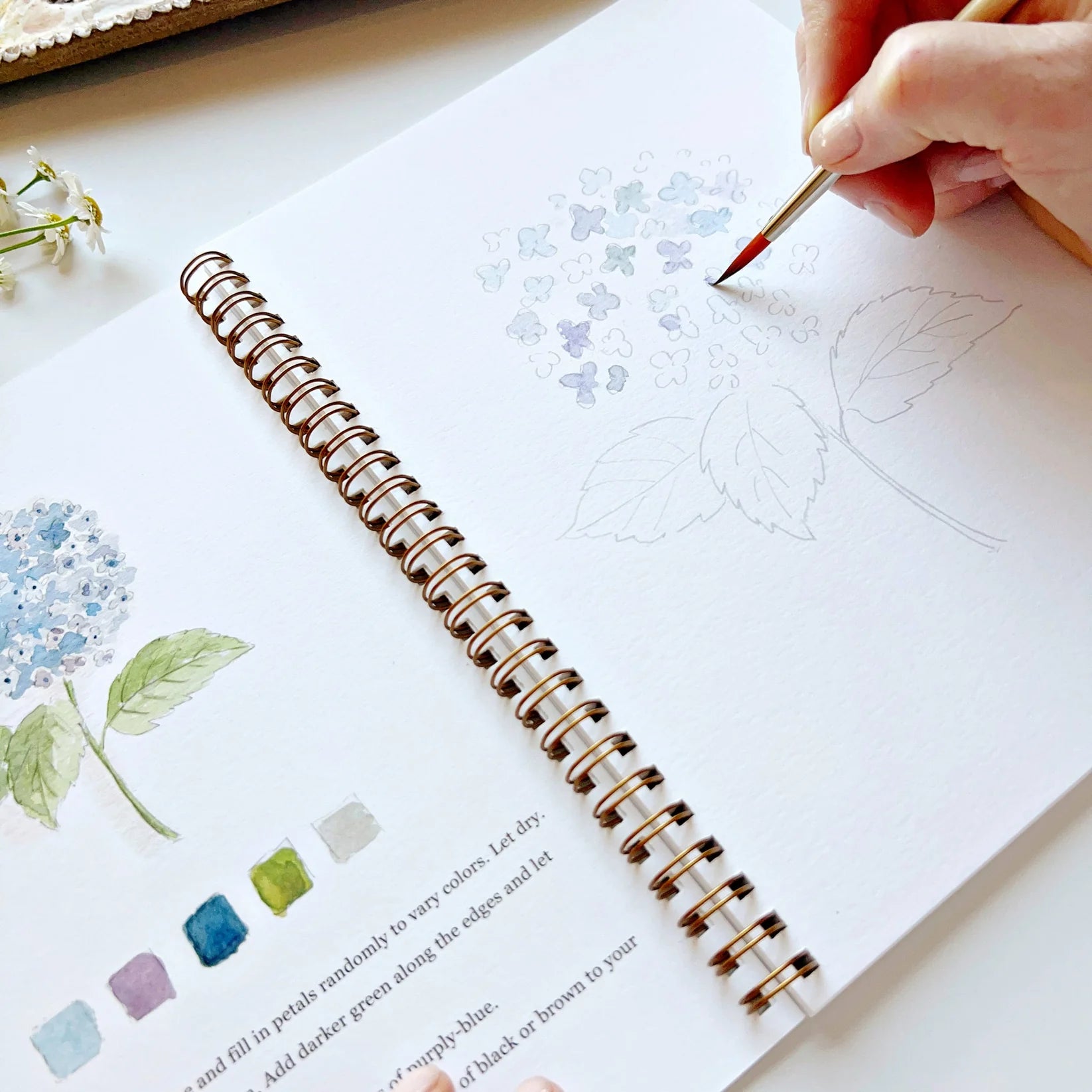 Person coloring a spiral-bound art book with a paintbrush