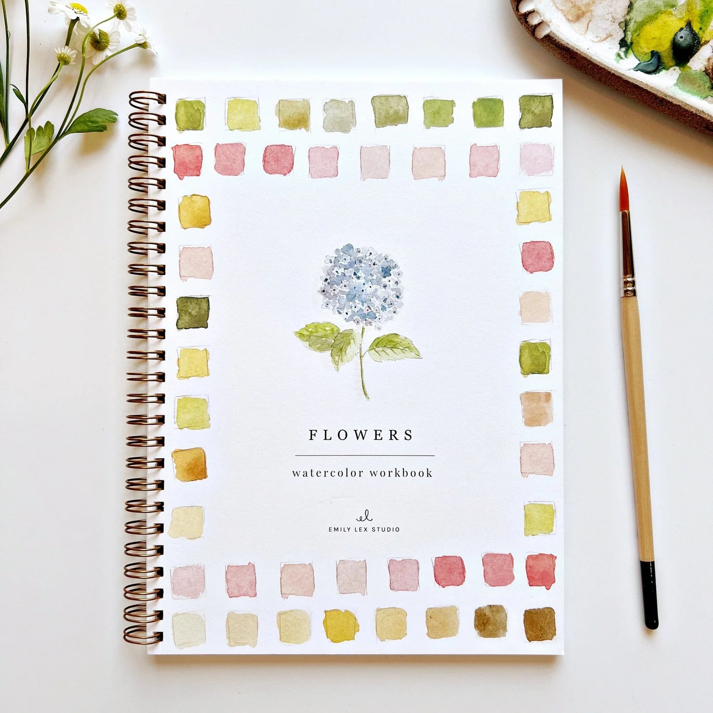 Watercolor workbook titled 'Flowers' by Emily Lex Studio on a white surface with a paintbrush and flowers.