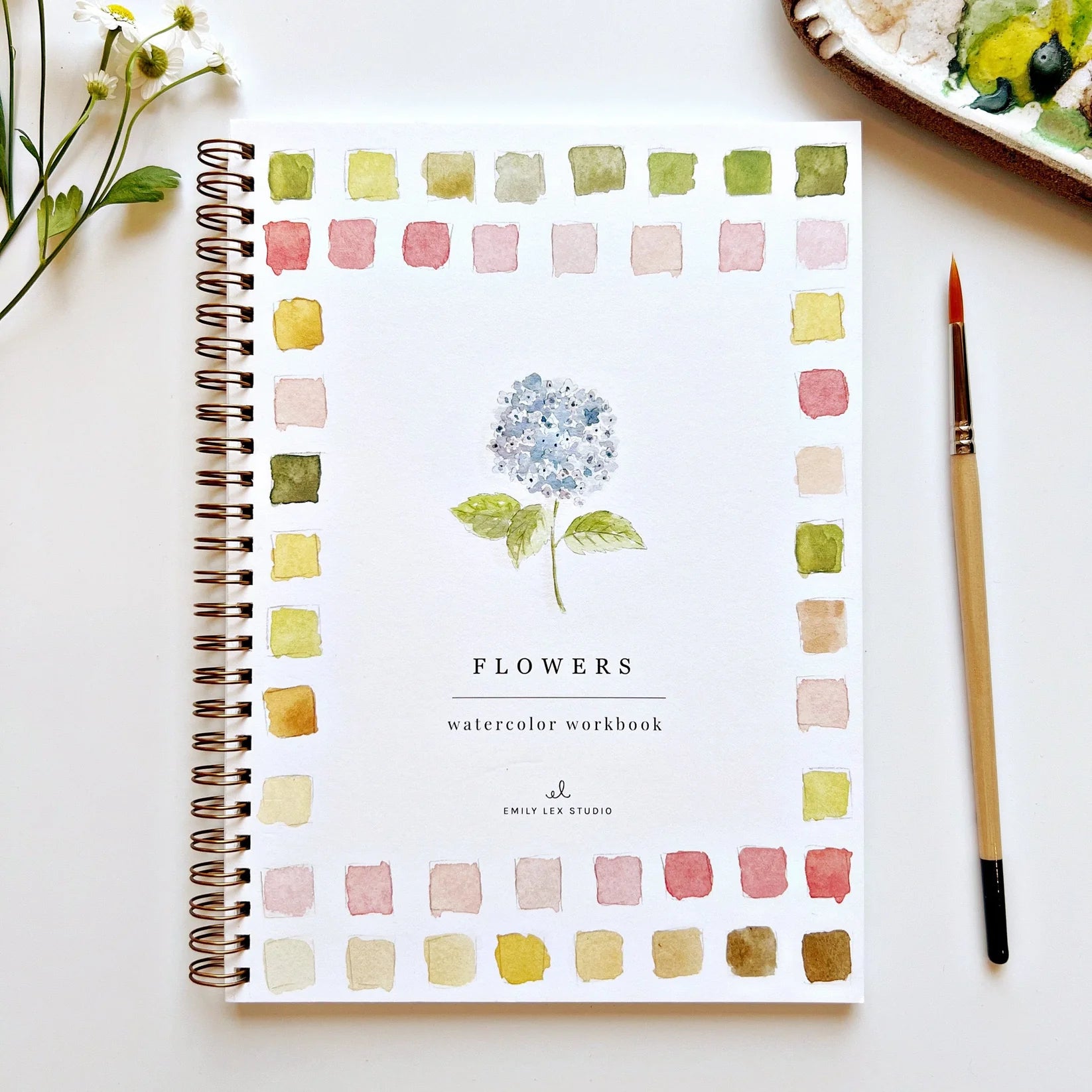 Watercolor workbook titled 'Flowers' by Emily Lex Studio on a white surface with a paintbrush and flowers.