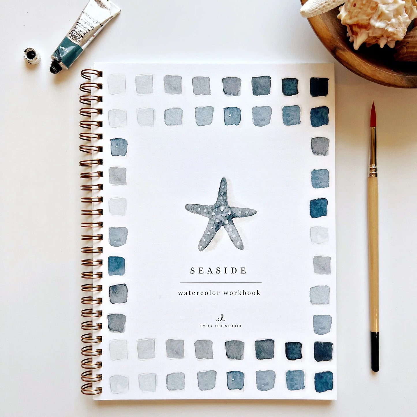Seaside-themed watercolor workbook with starfish design on a white surface with art supplies.
