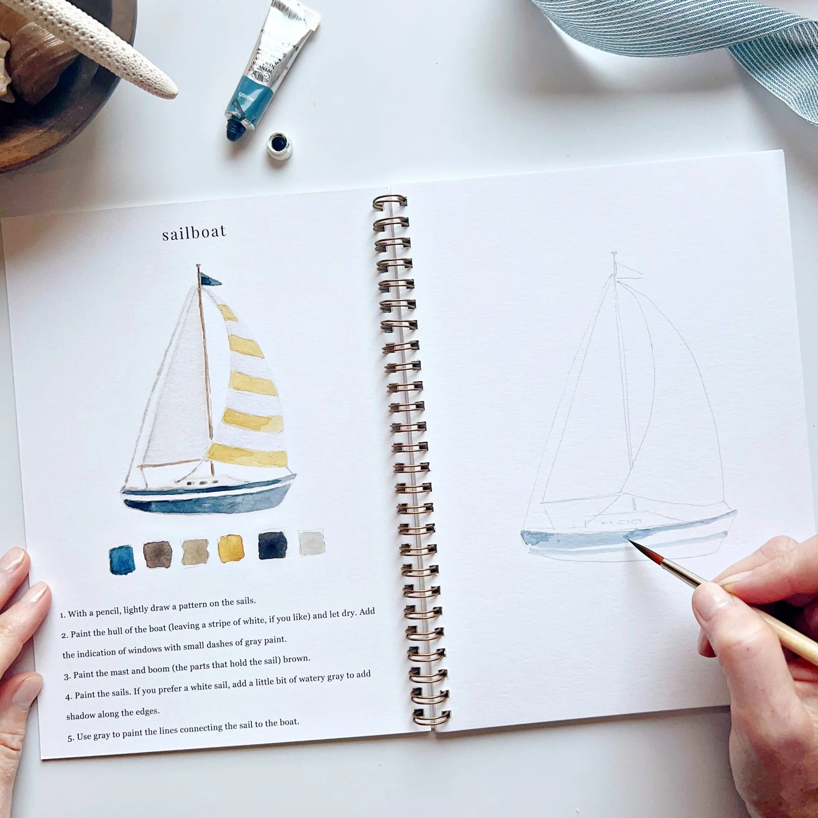 Person drawing a sailboat in a sketchbook with a color chart next to it.