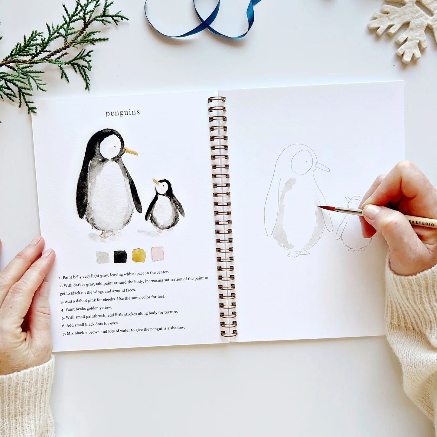 Person drawing penguins from a coloring book with a pen on a white surface.